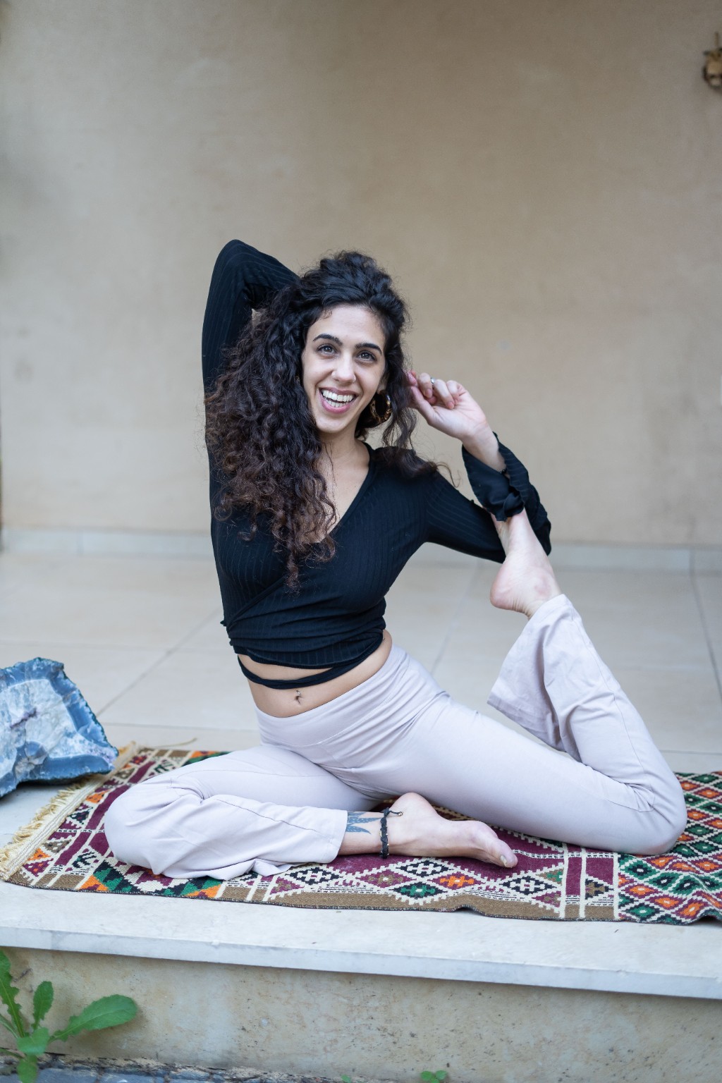 עדי מחייכת במהלך תרגול יוגה על מזרן